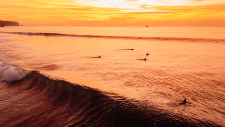 Golden sunset over ocean waves with surfers and bright sky