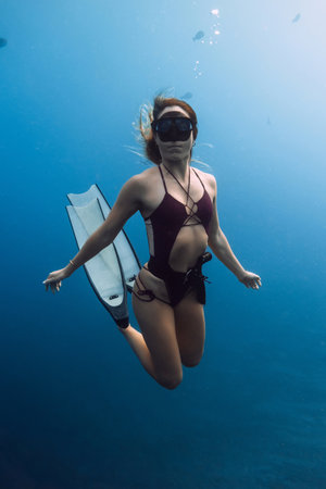 Attractive woman freediver gracefully swims underwater with freediving fins in blue oceanの写真素材
