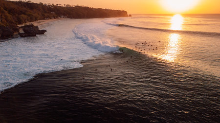 Surfers on Padang Padang surf spot on evening at sunset with perfect wavesの写真素材