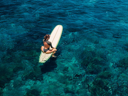 Woman on surfboard in blue ocean. Aerial view of woman during surfingの写真素材