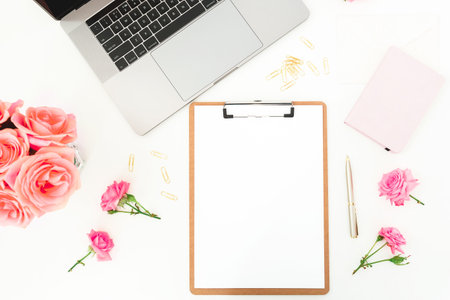 Stylish feminine workspace with laptop, clipboard and roses on white desk, creative home office flat layの写真素材