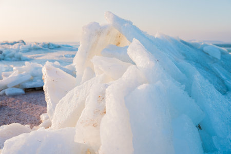 Frozen winter shoreline with stacked ice slabs at sunset