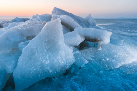 Stacked ice slabs on a frozen coastline at sunset with evening light and deep blue shadows.