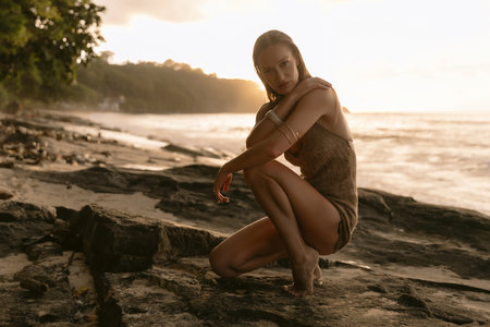 Beautiful young woman posing on rocky beach at sunset, natural light portrait