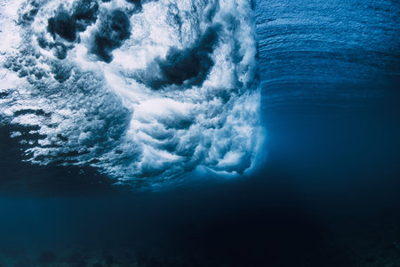 Underwater view inside crashing ocean wave, blue water with light rays and dramatic motion
