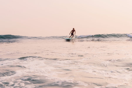 Surfer man riding a small wave at golden sunset. Surfing on longboardの写真素材
