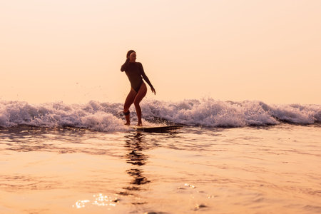 Woman on surfboard ride on foam wave with warm sunrise or sunset tones.の写真素材