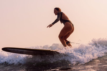 Attractive surfer girl in swimsuit rides on surfboard with warm sunlight. Woman on longboard on...