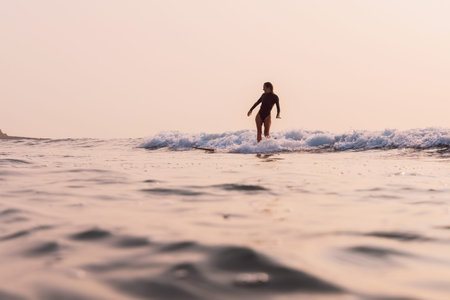 Surfer rides on surfboard on foam wave with warm sunrise .の写真素材