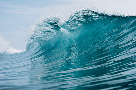 Powerful turquoise ocean wave breaking under blue sky, crashing barrel wave