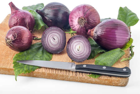 Group of red spanish onions and a kitchen knife on a worn cutting board.の写真素材