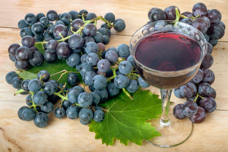 Ripe grapes with vine leaves and a glass of red wine on a rustic wooden board.の写真素材
