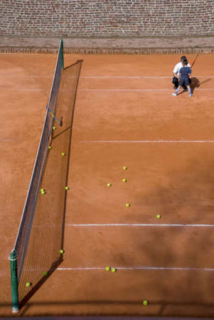 Tennis clay court with yellow tennis balls and net. A few words from a coach to talented child.の写真素材
