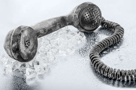 A frozen retro telephone receiver over the ice on a steel metal plate. Concept: "Hold The Line".の写真素材