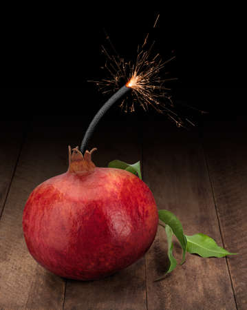 Red pomegranate with sparkler on dark wooden background. Vitamin Bomb Concept.の写真素材