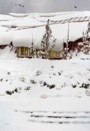 Heavy snowdrift covering house and slides off the roof.の写真素材
