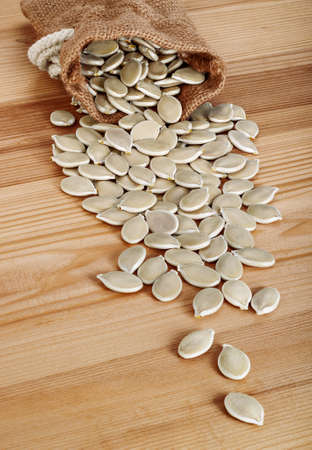 Dried pumpkin seeds spilling from a jute bag on wooden background.の写真素材
