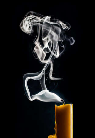 Extinguished candle with smoke and glowing wick on a black background.の写真素材