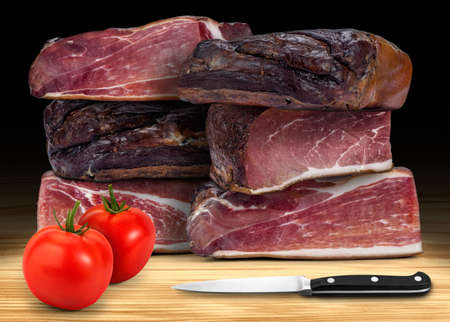 Italian prosciutto from Alps, with two tomatoes and kitchen knife, on wooden background. High resolution, low key image.の写真素材