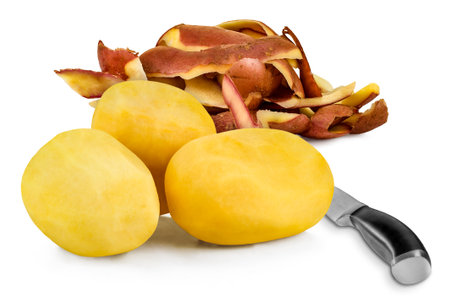 Three peeled potatoes (Solanum tuberosum) with a kitchen knife on a white background. Potato peel behind.の写真素材