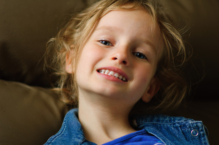 Portrait of a curly blue-eyed girl with a confident smile. She shows her white milk teeth.