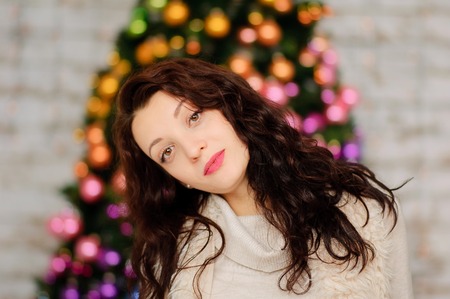 Portrait of Beautiful Young Woman with Long Dark Hair near Blurred Christmas Tree with Colorful Glass Balls.の写真素材