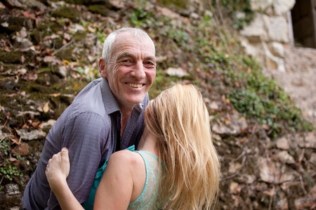 Handsome Senior Man Hugging His Young Girlfriend Outdoors and Smiling Looking at the Camera.の写真素材