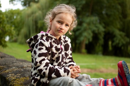 Portrait of a beautiful curly blue-eyed girl sitting on a background of green trees. Vacation in the village.の写真素材