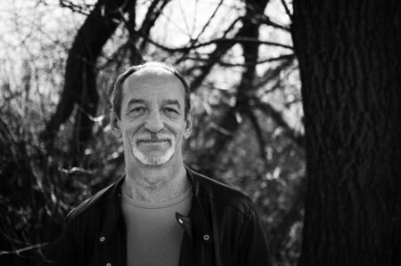 Black and white portrait of mature serious man with grey hair in dark leather jacket standing...