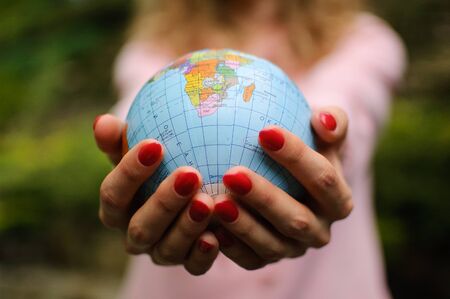 The girl in a pink sweater with red manicure holds a small globe with geographical names in Ukrainian cyrillic letters on it. African continent and Ocean are visible.の写真素材