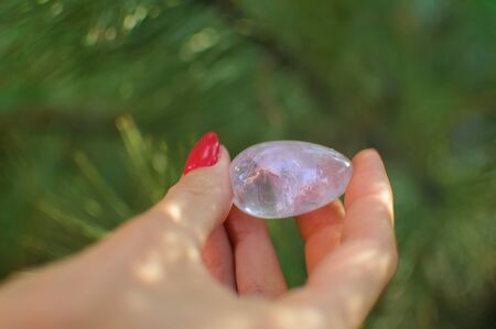Female hand with red manicure holding transparent violet amethyst yoni egg for vumfit, imbuilding or...