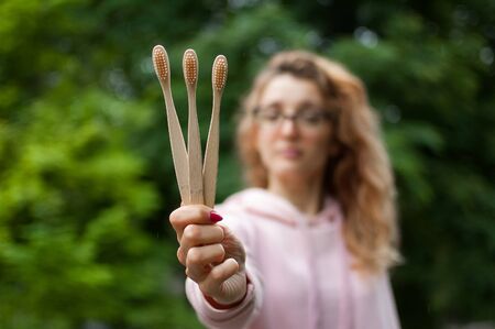 Outdoors portrait of young beautiful woman with blonde curly hair and eyeglasses holding three...