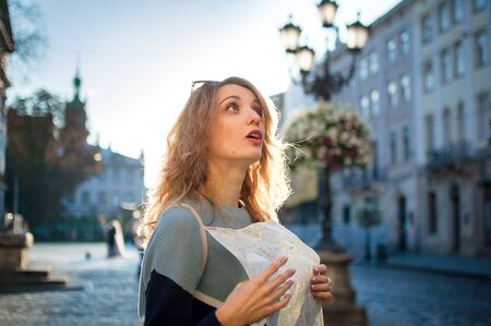 Happy excited adult girl is looking at the paper map and searching for direction early in the...