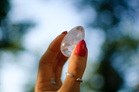 Female hand with transparent amethyst quartz yoni egg for vumfit, imbuilding or meditation. Shining crystal egg in hands on sky and sunrise background outdoors. Womens health concept.の写真素材