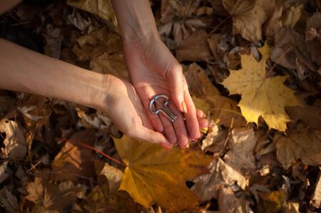 Female hands are holding traditional hutsul drymba or jews-harp, the oldest musician instrument in the world on fallen leaves background during autumn day outdoorsの写真素材