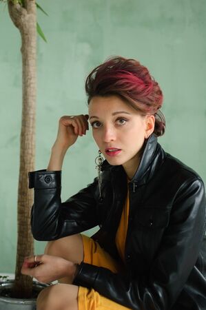 Glam rock style look of a beautiful girl with dark pink hair and mohawk wearing yellow dress and...