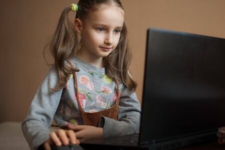 Serious little girl is concentrated in front of her black laptop while focused on doing homework...