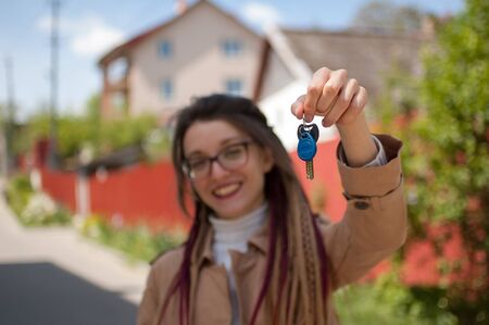 Cute smiling girl with long dreadlocks and eyeglasses showing bunch of house keys in a hand towards the camera. Real estate agent conceptの写真素材