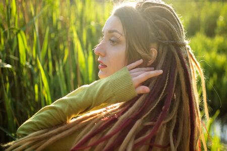 Outdoors portrait of a girl with dreadlocks and green shirt in a city park near the lake during a sunset, be free concept.の写真素材