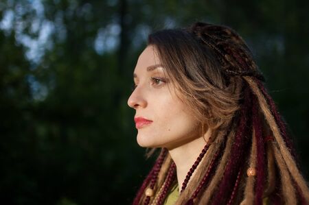 Outdoors portrait of a sensual girl with long dreadlocks wearing green shirt in a city park during a...