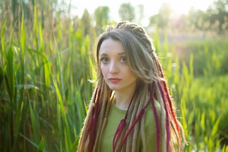 Outdoors portrait of a girl with dreadlocks and green shirt in a city park near the lake during a...