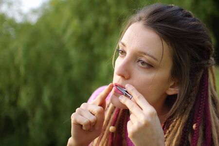 Close-up outdoors portrait of young female shaman in pink knitted sweater with long dreadlocks...