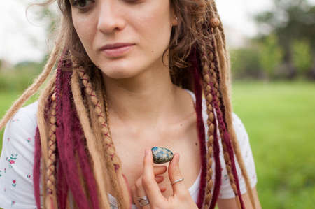 Young beautiful girl with long dreadlocks holds in hand azurite, natural stone outdoors during...