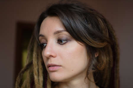 Indoors female portrait of a sensual girl with long dreadlocks and dark makeup with black eyeshadow,...