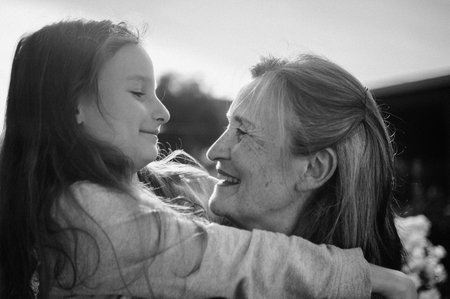 Black and white portrait of senior grandmother with gray hair with her little granddaughter hugging in the garden and during sunny day outdoors, mothers dayの写真素材