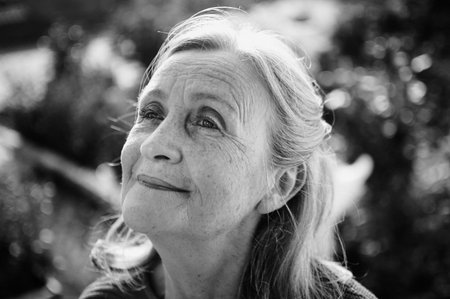 Black and white portrait of senior woman with grey hair and face with wrinkles outdoors relaxing at the parkの写真素材