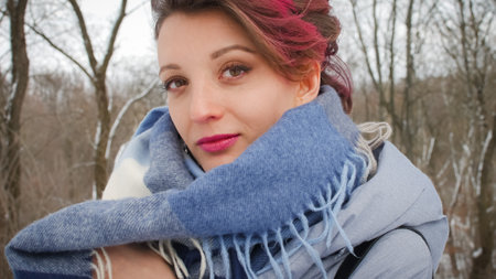 Attractive young woman with perfect skin and makeup with dark pink hair is possing on winter park background wearing blue scarf and silver earringsの写真素材
