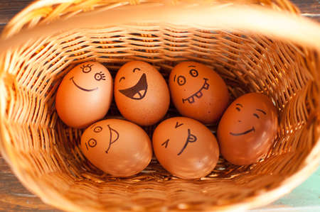Stack of eggs with hand drawn faces on straw basket, easter preparation, holiday mood concepts