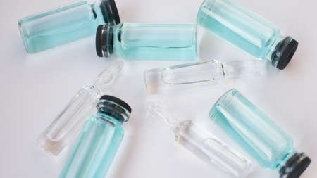 Vial vaccine, top view of glass ampoules with transparent and blue liquid lying on white background,...