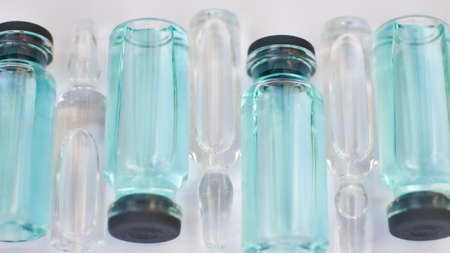 Vial vaccine, top view of glass ampoules with transparent and blue liquid lying on white background,...